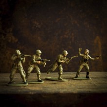 Four toy soldiers stand in various combat stances, ready for action on a weathered wooden surface.