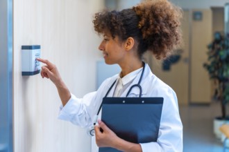Confident female doctor using a keypad to enter a code, holding a clipboard in a hospital corridor