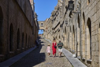 Tourists walking through a sunny, stony alley, Knights Street, Rhodes Old Town, Rhodes, Dodecanese,