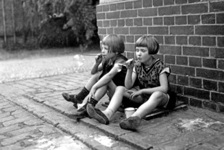 Two girls playing with soap bubbles, 1920s, Two children sitting on a brick wall and blowing soap