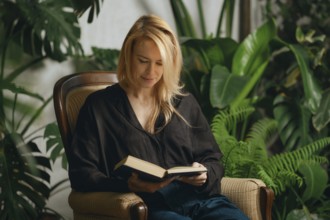 In a serene indoor setting filled with lush green plants, a woman with long blonde hair sits