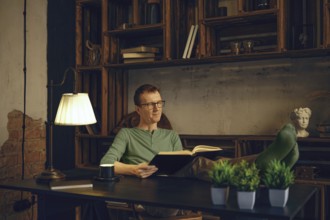 A person sits comfortably in a modern workspace, immersed in a book. Soft lamp light creates a warm
