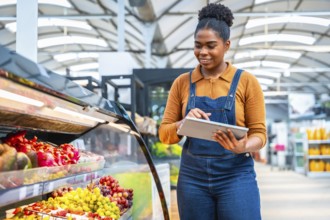 Smiling african supermarket employee using digital tablet checking products freshness and managing