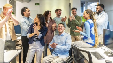 Happy business team celebrating success, clapping and congratulating a colleague in a wheelchair