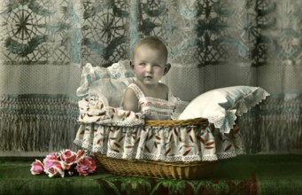 Baby in a basket, 1920s, A toddler sits cosily in a bassinet, surrounded by floral details,