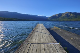 A wooden jetty stretches into a clear blue lake surrounded by majestic mountains, Summer, Lake