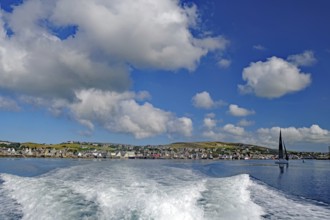 View of the sea with wave foam and boats in front of a town under a blue sky, Stromness, Mainland,