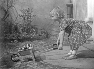 Girl with wheelbarrow, 1920s, A girl playing in the garden with a wheelbarrow, Historical photo
