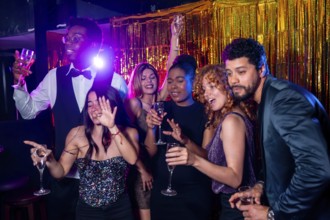 Group of cheerful elegant friends having fun together and drinking sparkling wine while dancing and