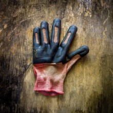 A single gardening glove lies on a rustic wooden surface, showing signs of wear and dirt from