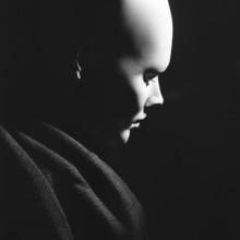 A smooth, featureless bust of mannequin head presented in profile against a dark background