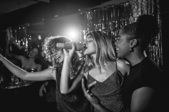 Group of friends singing joyfully during karaoke night, enjoying each other's company and creating