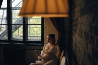 In a cozy room filled with natural light, a pregnant woman sits comfortably on sofa and making