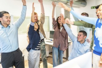 Multicultural businesspeople celebrating success in a bright office, raising arms in unity,