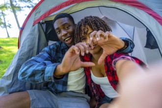 Young smiling couple making heart shape with hands taking selfie inside tent during camping trip