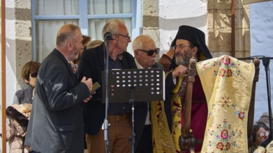 Several men, including priests, discussing in front of a crowd, one holding a microphone,
