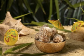Coconut, bowl filled with sweet confectionery on sand, decorated with yellow umbrellas