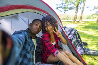 Young couple taking a selfie inside their tent while camping in nature, enjoying a relaxing