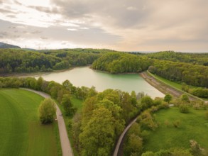 Spring in nature with a forest lake and paths under a cloudy sky, Glems reservoir, Swabian Alb,