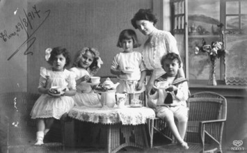 Mother with children around a coffee table, 1920s, Four children and a woman enjoying a tea party