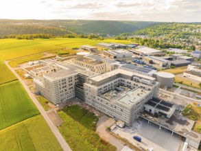 Large industrial complex with multi-storey buildings and surrounding fields and hills, construction