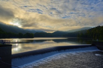 Sunrise over a reservoir, Paulushof dam, dam with flowing water, cloudy sky and mountains, summer,