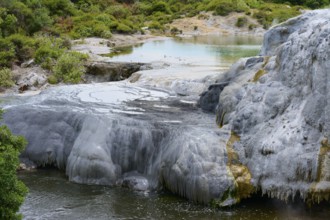 White mineral deposits and rock formations surround a geothermal spring with clear water and dense