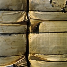 A large stack of compressed paper products is arranged in a recycling area. The paper displays wear