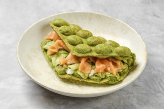 A vibrant green matcha waffle sandwich is filled with fresh salmon, crisp vegetables, and creamy