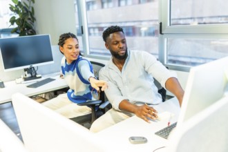 Two colleagues are working together in a modern office, discussing a project on a computer,