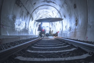 An illuminated tunnel with rails and graffiti on the walls. In the background is a figure with a