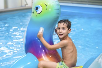 Smiling boy having fun riding an inflatable toy whale in a home swimming pool, enjoying summer