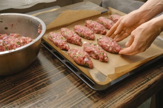 Hands shape meat patties on a lined baking tray in a warm kitchen. This preparation hints at a