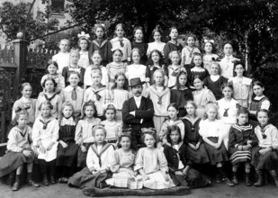Class photo of a girl teacher, ca. 1910, group of pupils and a teacher posing together outdoors,