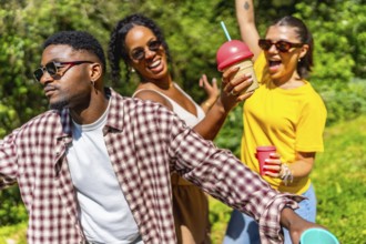 Three friends enjoying summer sunshine, dancing joyfully while sipping cold drinks and sharing