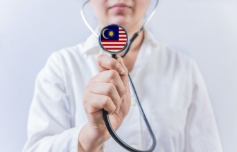 Female doctor holding stethoscope with Malaysia flag. National health system of Malaysia
