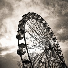 A towering Ferris wheel emerges against a swirling, moody sky during twilight hours, evoking