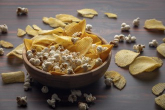 Wooden bowl with crisps and popcorn scattered on the table