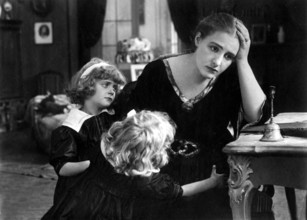 Overwhelmed mother, 1920s, A woman looks worried while two children hug her in a gloomy room,