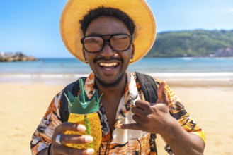 Young man enjoying summer vacation on a tropical beach, holding a pineapple shaped cocktail and