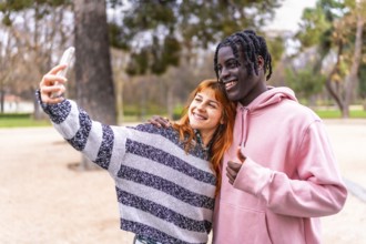 Happy multi ethnic couple enjoying a sunny day in the park, taking a cheerful selfie while flashing