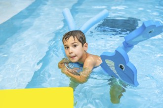 Happy boy playing with inflatable toy whale in swimming pool during summer vacation, enjoying