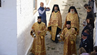 Clerics in richly decorated robes walk along a stone alley, spectators take photos, Orthodox