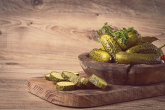 Pickled cucumbers in a wooden bowl with herbs and spices, close-up, rustic style