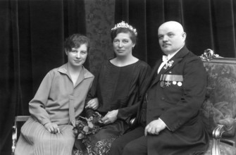 Family with a child, 1920, Two woman and a man in formal dress on a sofa, the man with medals,