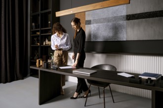 Two women engage in a thoughtful discussion in a sleek office setting. One takes notes on a