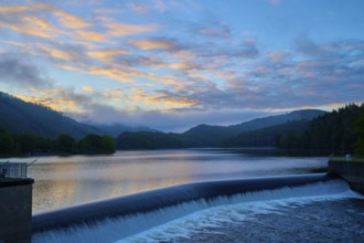 Atmospheric dam Paulushof-Absperrdamm, and lake at dusk, surrounded by mountains and trees under a