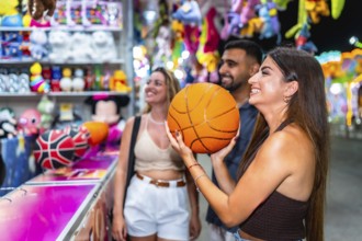 Group of friends enjoying a lively evening at a funfair game stall, celebrating their basketball