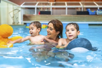 Smiling mother enjoying time with her sons while swimming in an indoor pool, playing joyfully with