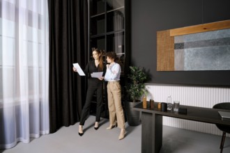 Two businesswomen discussing documents in a modern office environment during the afternoon